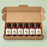 An open kraft cardboard gift box containing five small dark glass bottles with white labels reading 'Vigorous Herbal' and '500 mg'. The bottles are arranged in brown crinkle paper packing on a pale mint green background.
